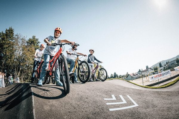 Schüler*innen am Starthügel eines Pumptracks. Sie sitzen auf Rädern und haben Helm auf. 